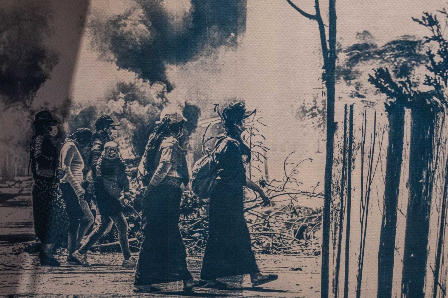 Gran cianotipo sobre papel en el que un grupo de mujeres indígenas camina entre humo y ramas quemadas