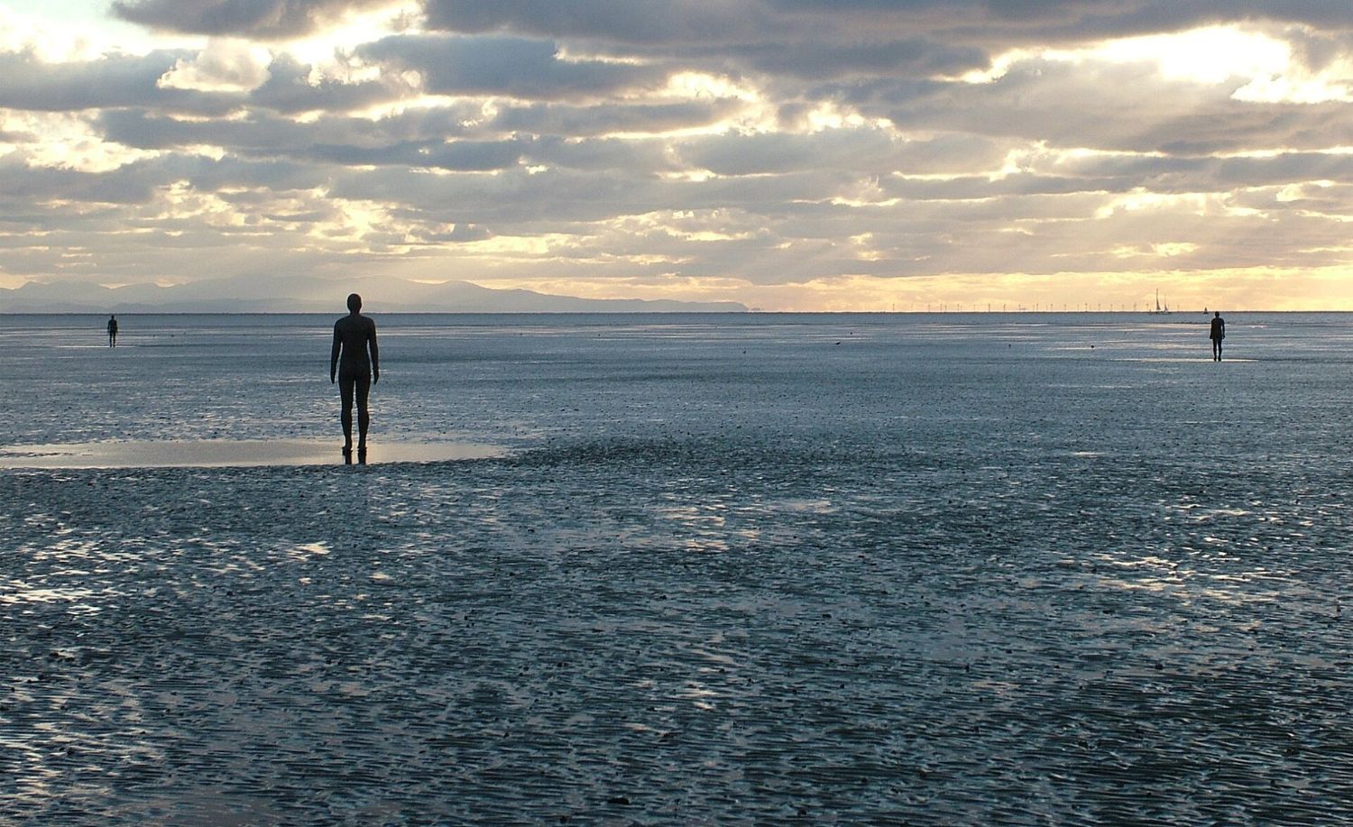 Antony Gormley, Another Place: figura de hierro en la playa frente al horizonte, con la marea baja