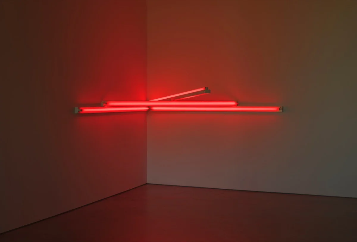 Obra de Dan Flavin en el ángulo de dos paredes: tubos fluorescentes rojos dispuestos en horizontal y en diagonal que bañan de rojo el rincón de la sala