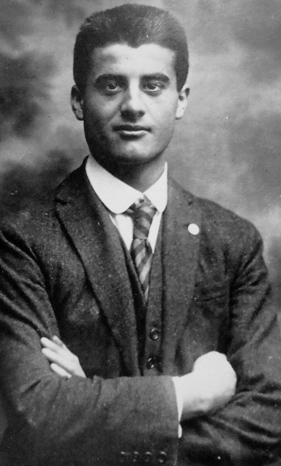 Retrato fotográfico de Pier Giorgio Frassati, joven, con traje y corbata, los brazos cruzados