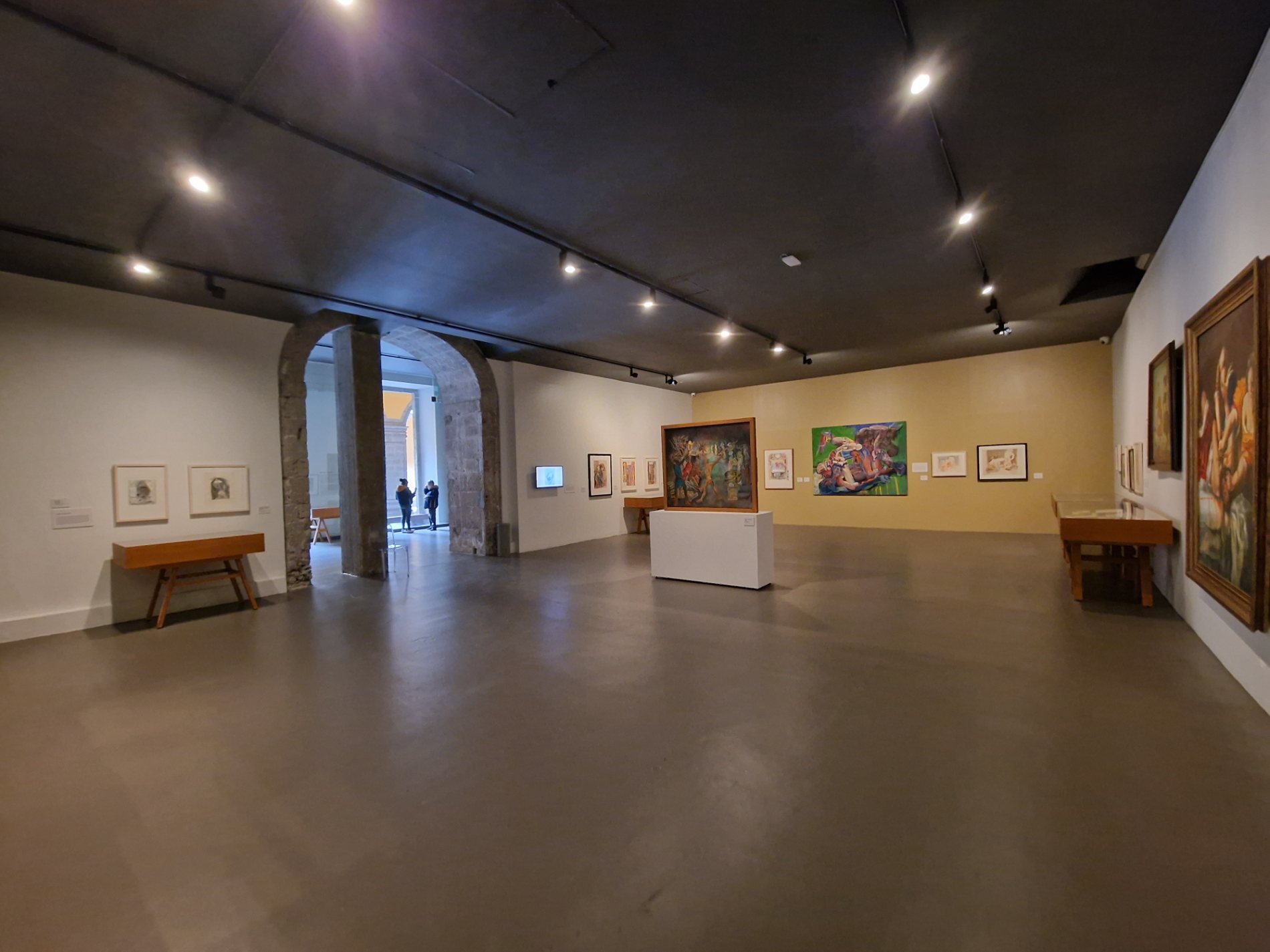 Sala de exposición temporal con un arco de piedra del antiguo colegio