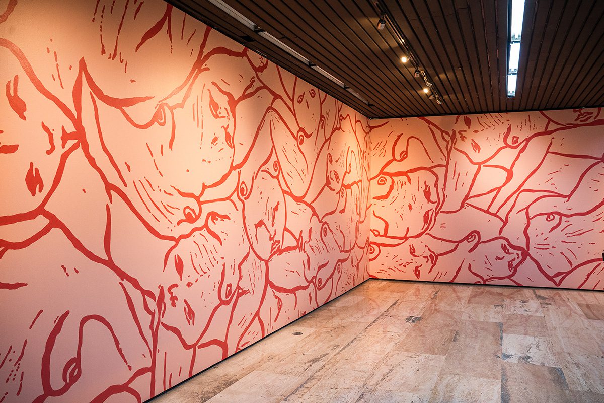 Sala con un mural de trazo rojo sobre fondo rosa que cubre dos paredes enteras